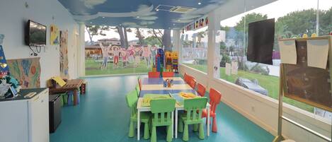 A classroom with a large table, colorful chairs, and artwork on the walls.