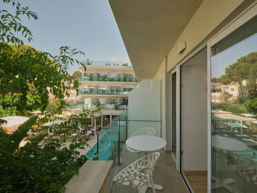 A balcony with a glass door, a pool area with lounge chairs, and a view of a building with multiple floors and outdoor seating.