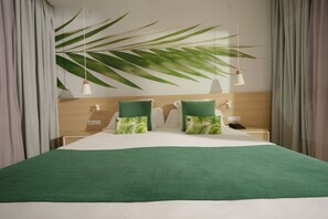 Una habitación de hotel con una cama, dos mesitas de noche, un teléfono y una planta grande.