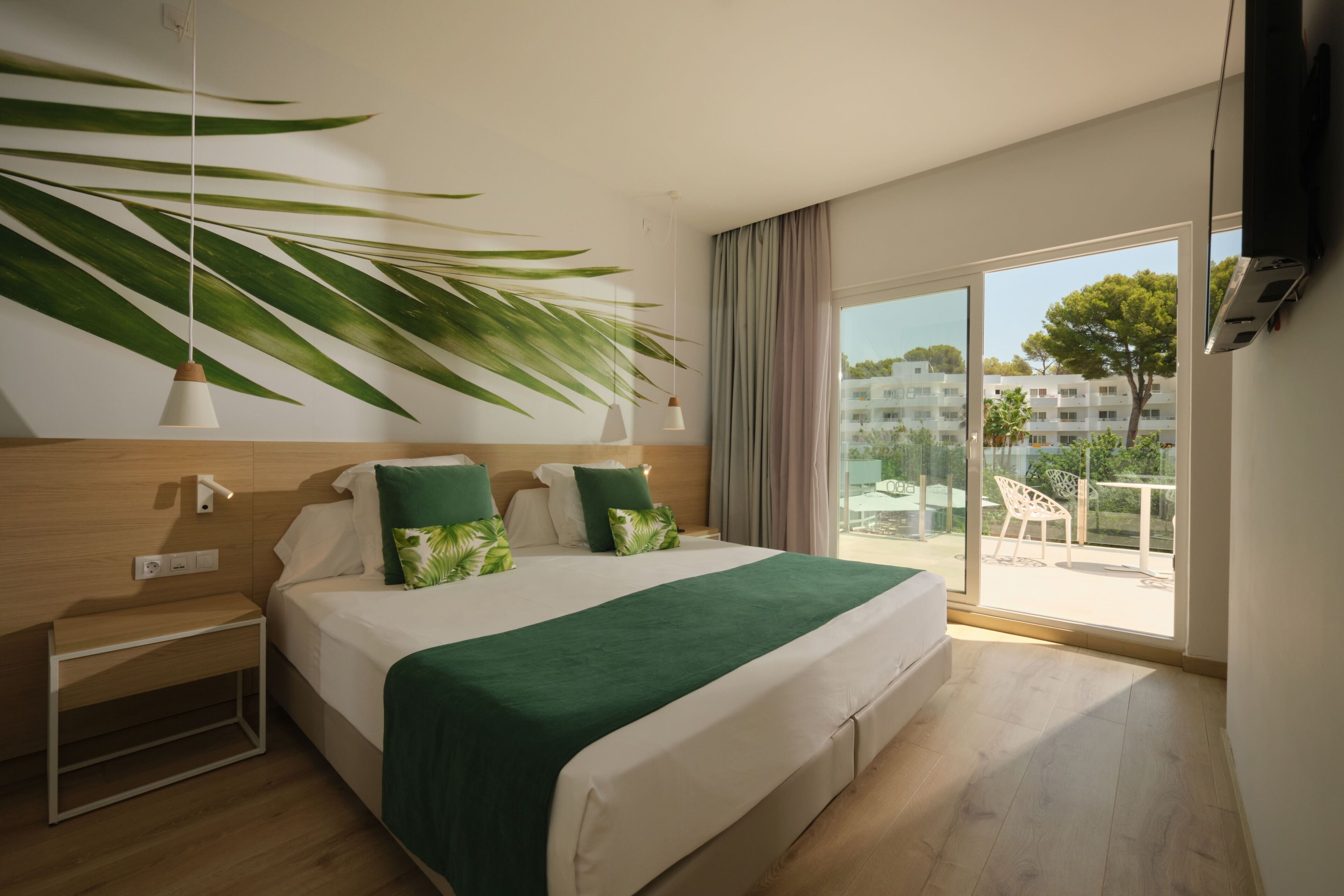 Habitación de hotel con cama, mesitas de noche, televisor y un amplio ventanal con vistas al exterior.