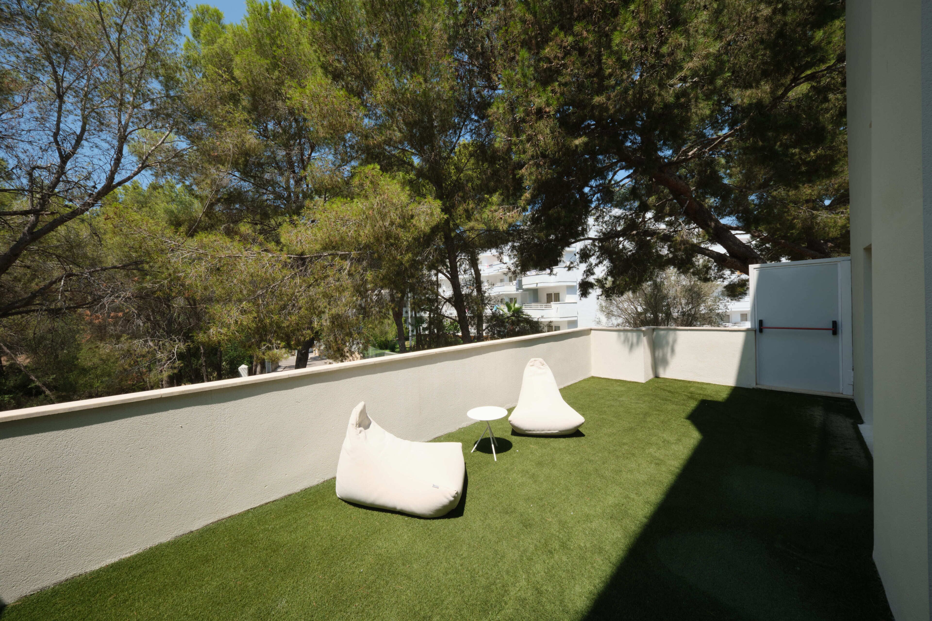 Una terraza en la azotea con césped artificial, dos pufs blancos y una pequeña mesa redonda.