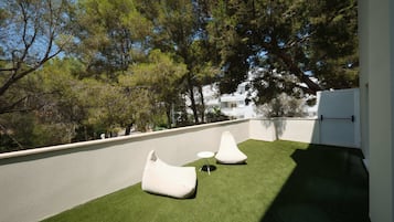 Una terraza en la azotea con césped artificial, dos pufs blancos y una pequeña mesa redonda.