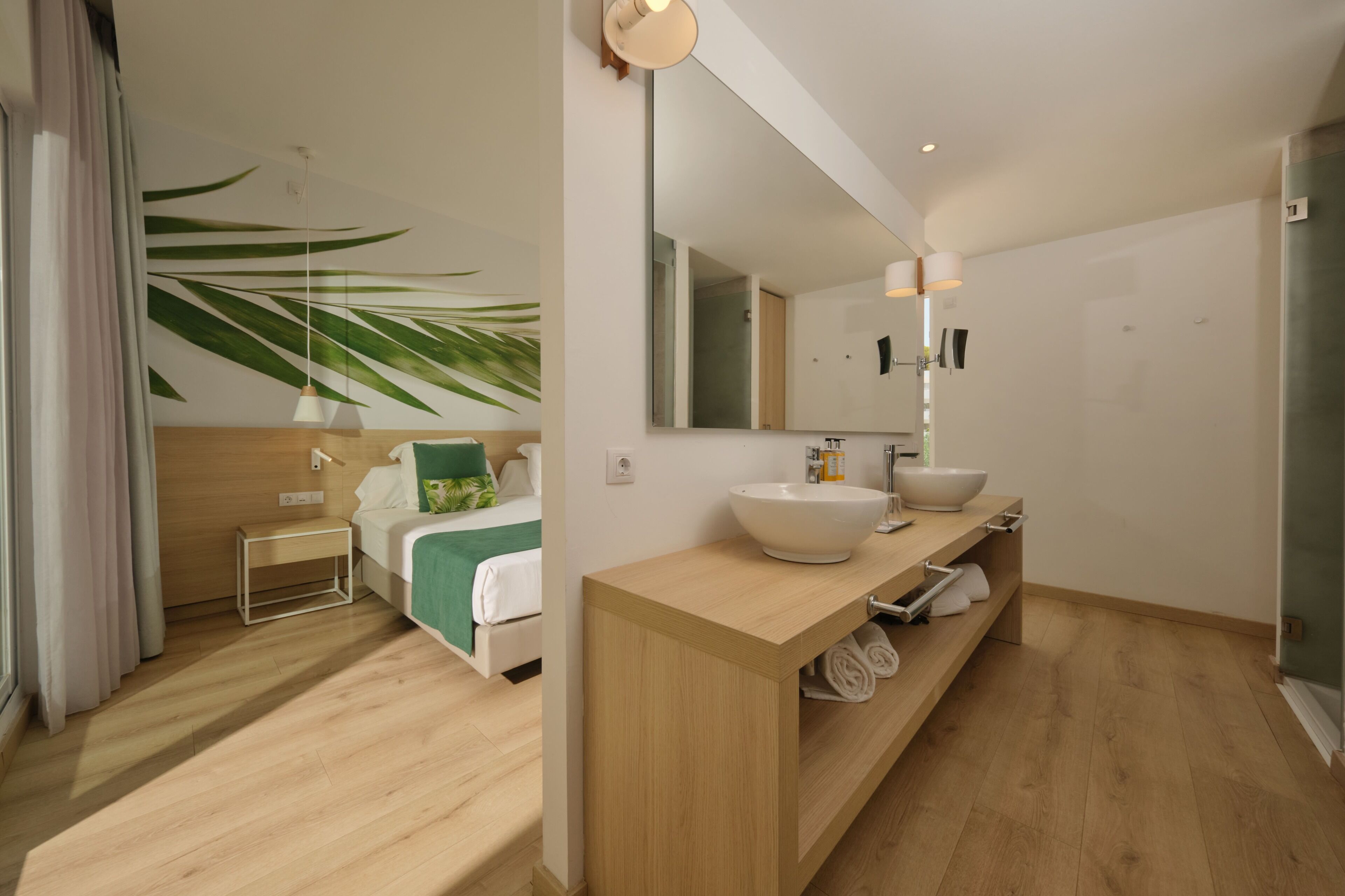 Een moderne hotelkamer met een bed, nachtkastje en een grote spiegel boven een houten wastafel.