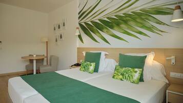 Une chambre d’hôtel avec un grand lit, deux oreillers, un bureau, une chaise et une plante fixée au mur.