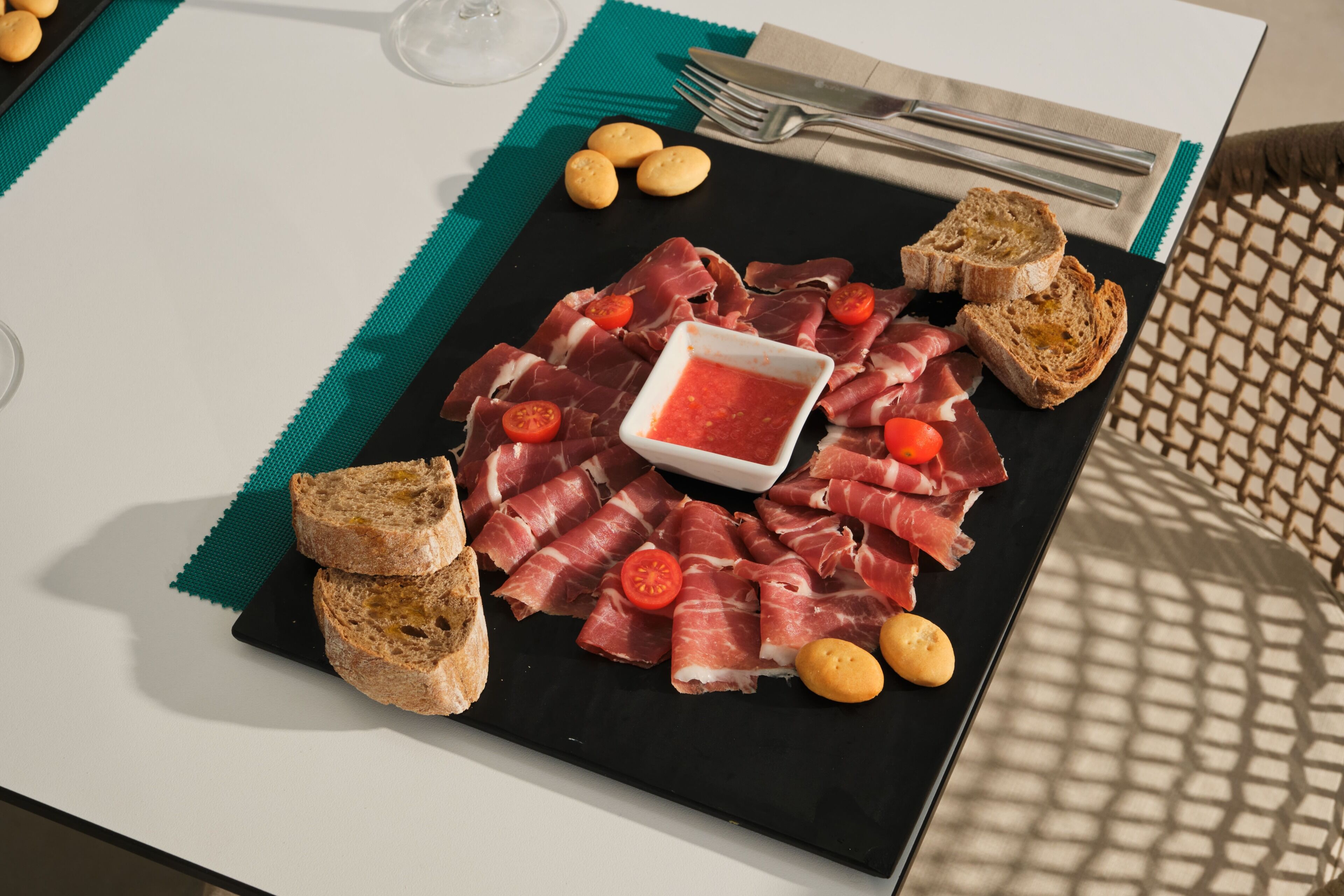 Un plato negro con varias carnes, pan y un recipiente pequeño con salsa.