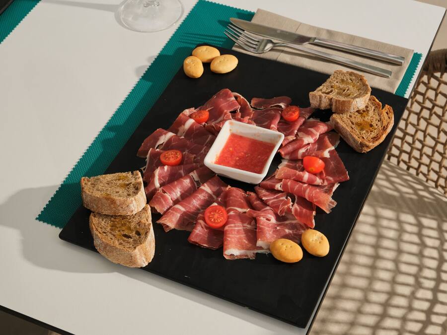 Un plato negro con varias carnes, pan y un recipiente pequeño con salsa.