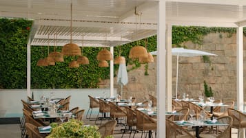 Un espace de restauration en plein air avec des chaises et des tables en osier, des lampes en osier suspendues et un mur végétal luxuriant.