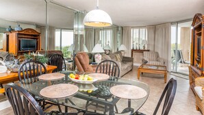 Un salon spacieux avec une table à manger en verre, des sièges confortables et une grande fenêtre donnant sur un paysage agréable.