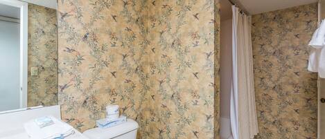 A bathroom with floral wallpaper, a toilet, a sink, and a shower curtain.