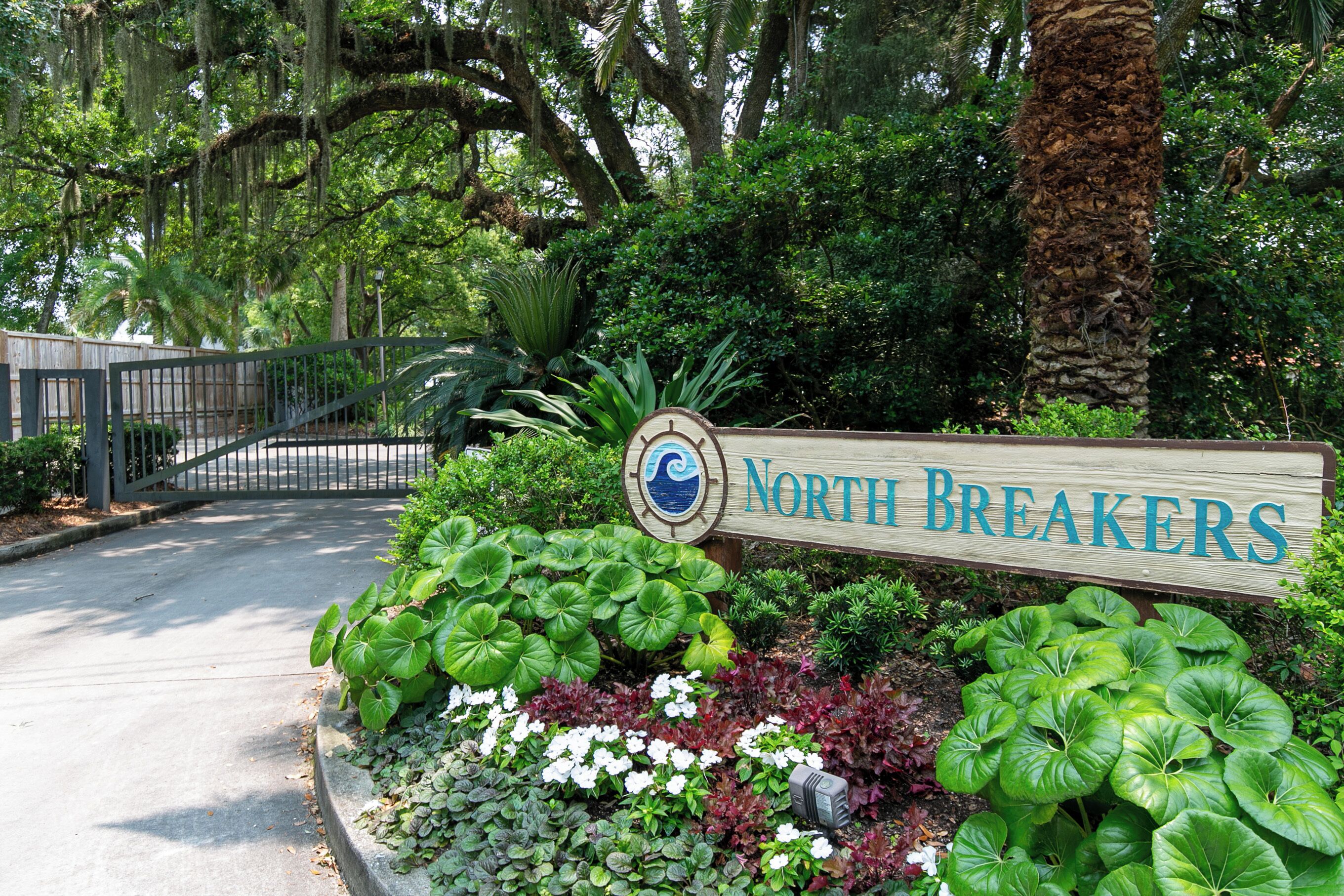 Une enseigne pour « North Breakers », avec un panneau en bois, entourée d’une végétation luxuriante et d’un palmier.