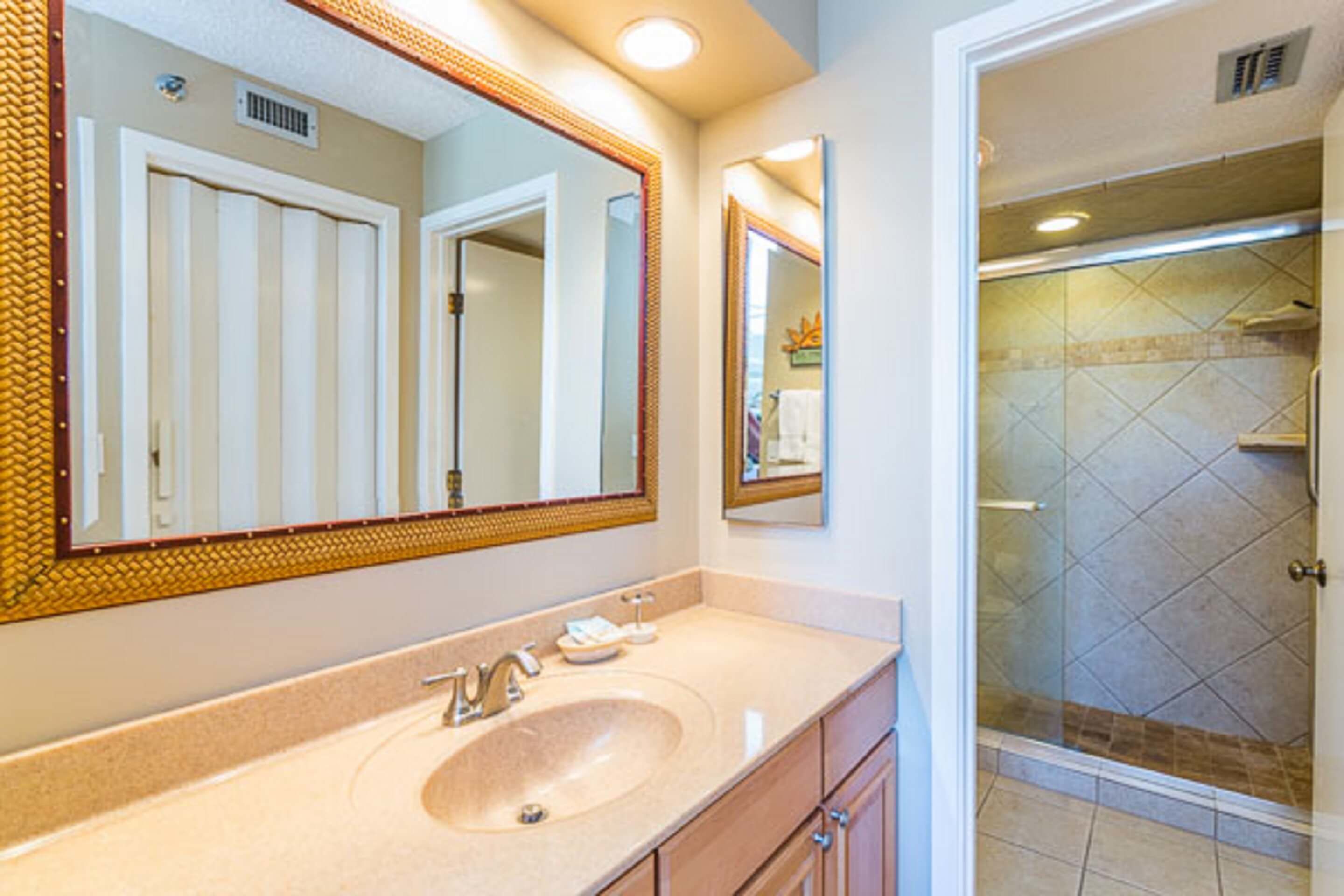 A bathroom with a large mirror, a sink, and a shower area.
