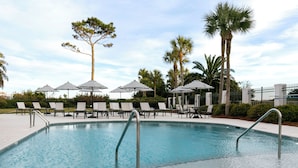 Une piscine entourée de palmiers et d’une clôture, avec des chaises longues et des parasols.