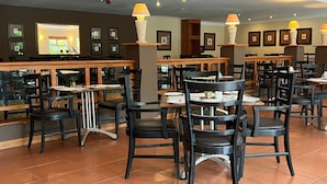 Un restaurant doté de nombreuses tables et chaises, de tableaux encadrés aux murs et d’un espace bar.