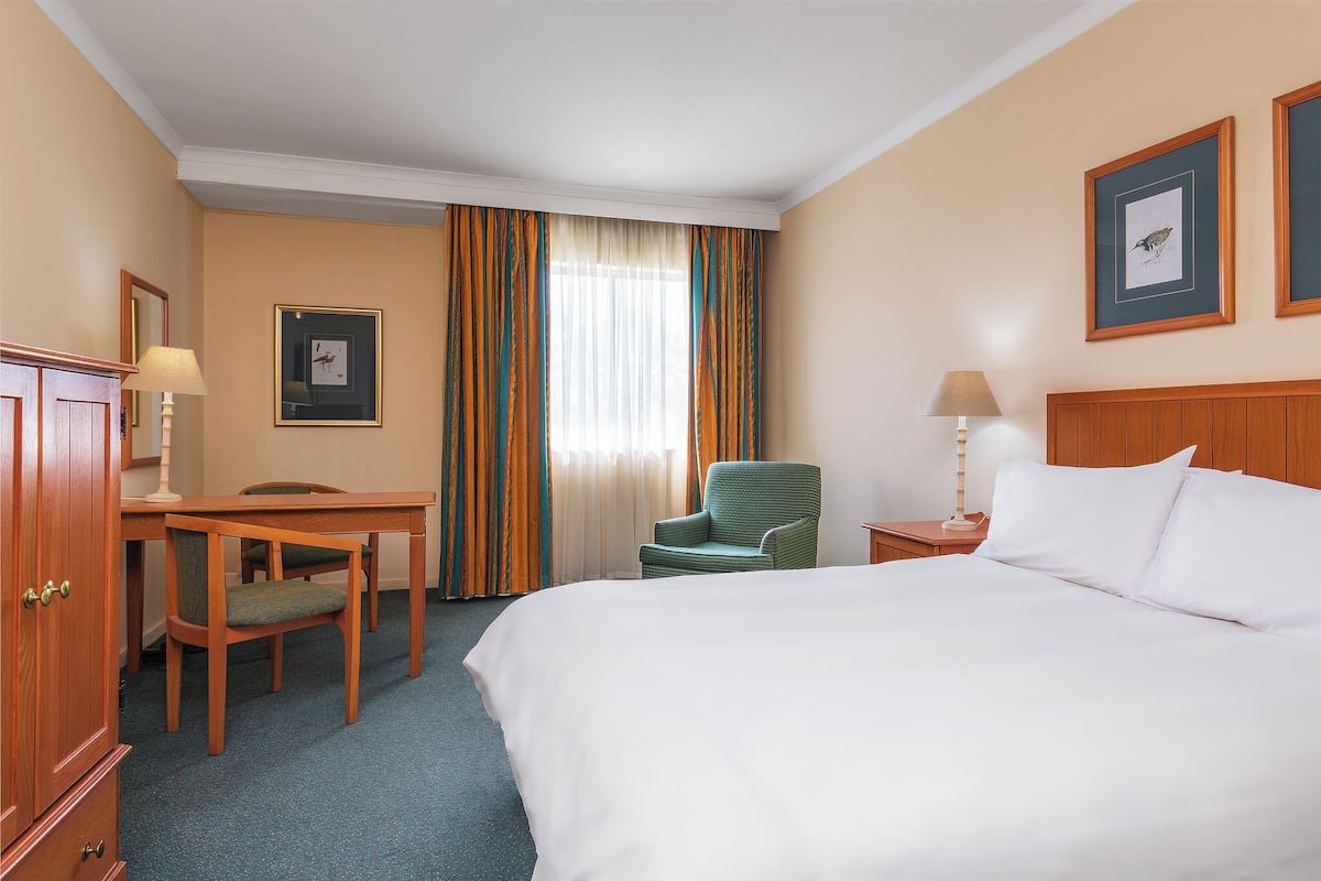 A hotel room with a bed, a desk, a chair, a nightstand, a lamp, and curtains.