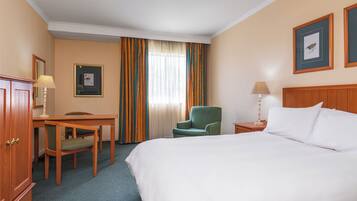 Habitación de hotel con cama, escritorio, silla, mesita de noche, lámpara y cortinas.
