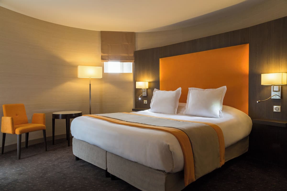 Een hotelkamer met een groot bed, twee nachtkastjes, een stoel en een lamp.