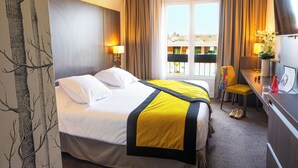 A hotel room with a large bed, a desk, a chair, a TV, and a window with curtains.
