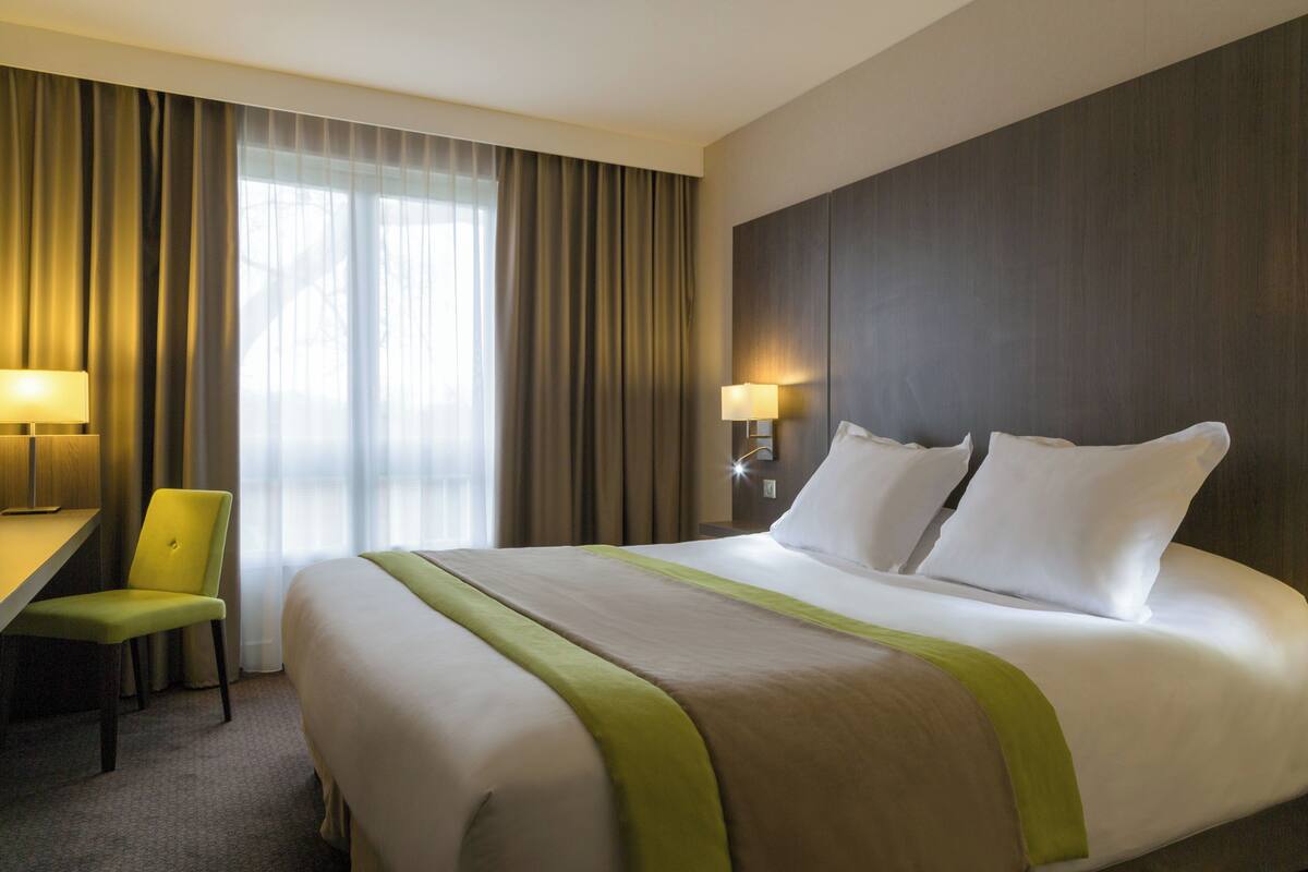 Een hotelkamer met een bed, een bureau, een stoel en een lamp.