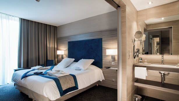 A modern hotel room with a large bed, bedside lamps, a vanity with a mirror, and a small trash bin.