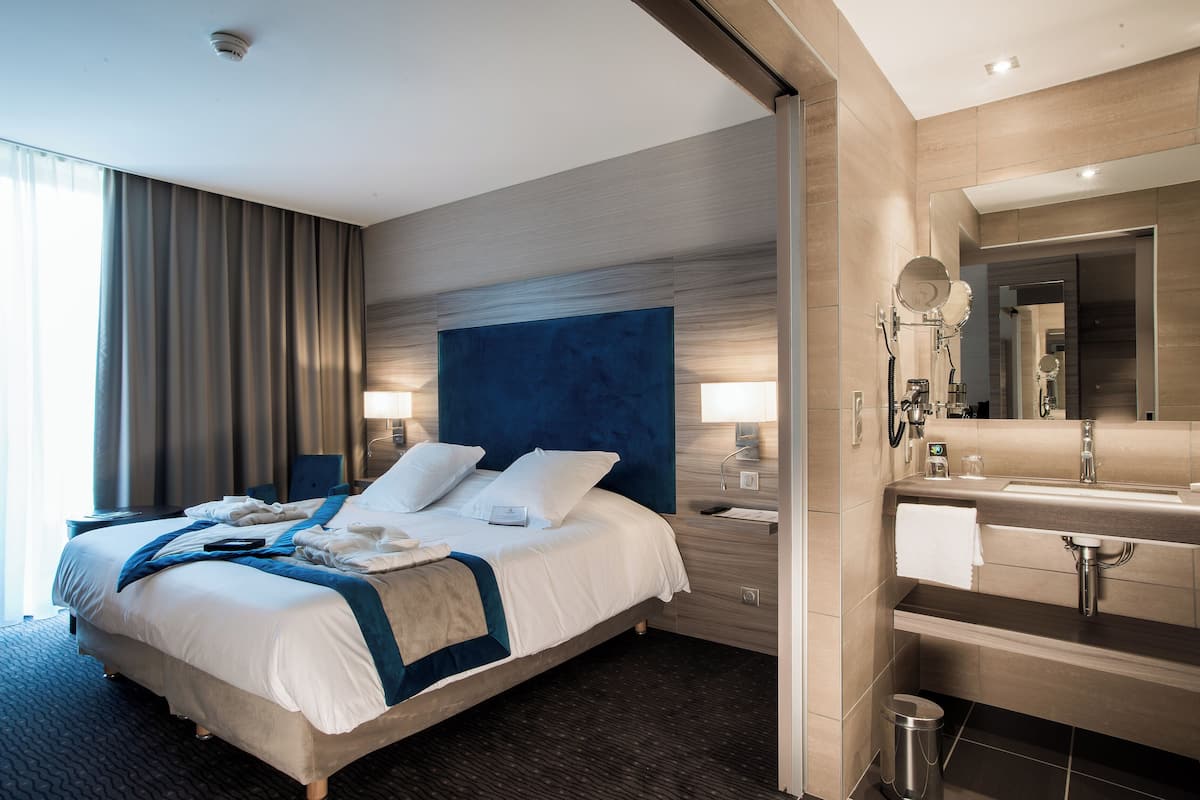 Een moderne hotelkamer met een groot bed, bedlampjes, een kaptafel met spiegel en een kleine prullenbak.