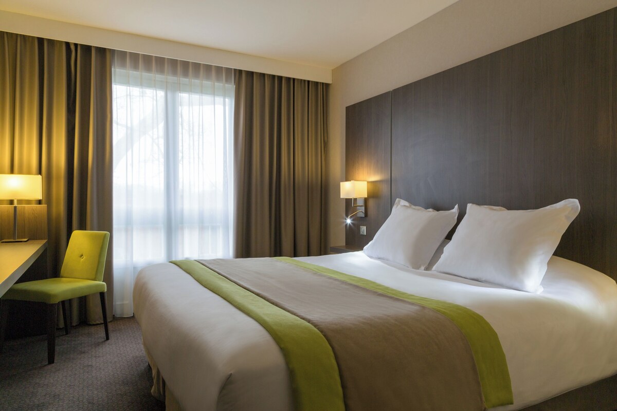 Une chambre d’hôtel avec un lit, un bureau, une chaise et une lampe.