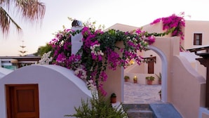 A building with a white facade, a wooden door, and a stone staircase leading to a covered area with potted plants. - Hotel Mathios Village (Santorini)