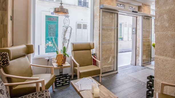 A lobby with two leather chairs, a wooden table with papers and candles, and a large window with a teal door. - Hotel Prince Albert Wagram (Paris)