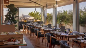 Un espacio de comedor al aire libre con mesas y sillas de madera, una barra de buffet y ventanas amplias con vistas a la ciudad.