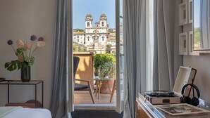 Habitación de hotel con cama, escritorio con computadora portátil, mesa de centro con planta y vista a una iglesia por la ventana.
