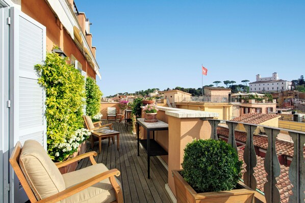 A balcony with wooden chairs and tables, surrounded by potted plants and a view of the cityscape. - Portrait Roma - Lungarno Collection (Rome)