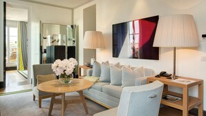 Una habitación de hotel moderna con un sofá, una mesa redonda con un florero, una lámpara y una mesita de noche con un teléfono y una revista.
