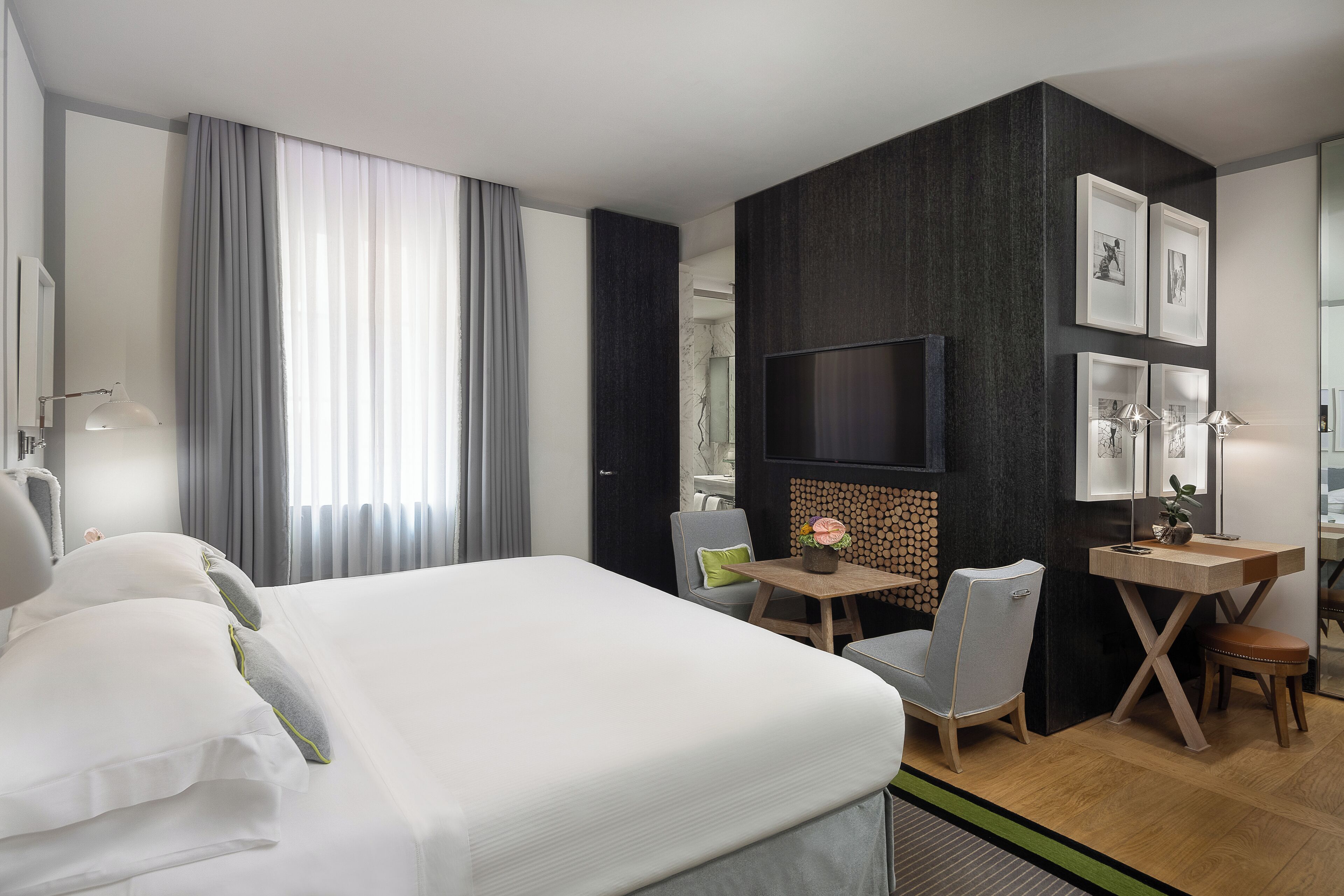 Quarto de hotel moderno com uma cama grande, uma escrivaninha, uma cadeira e uma televisão.