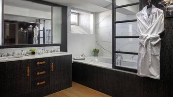 A modern bathroom with a large mirror, a bathtub, and a robe hanging on the wall.