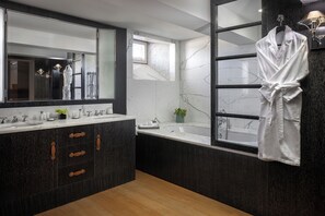 A modern bathroom with a large mirror, a bathtub, and a robe hanging on the wall.