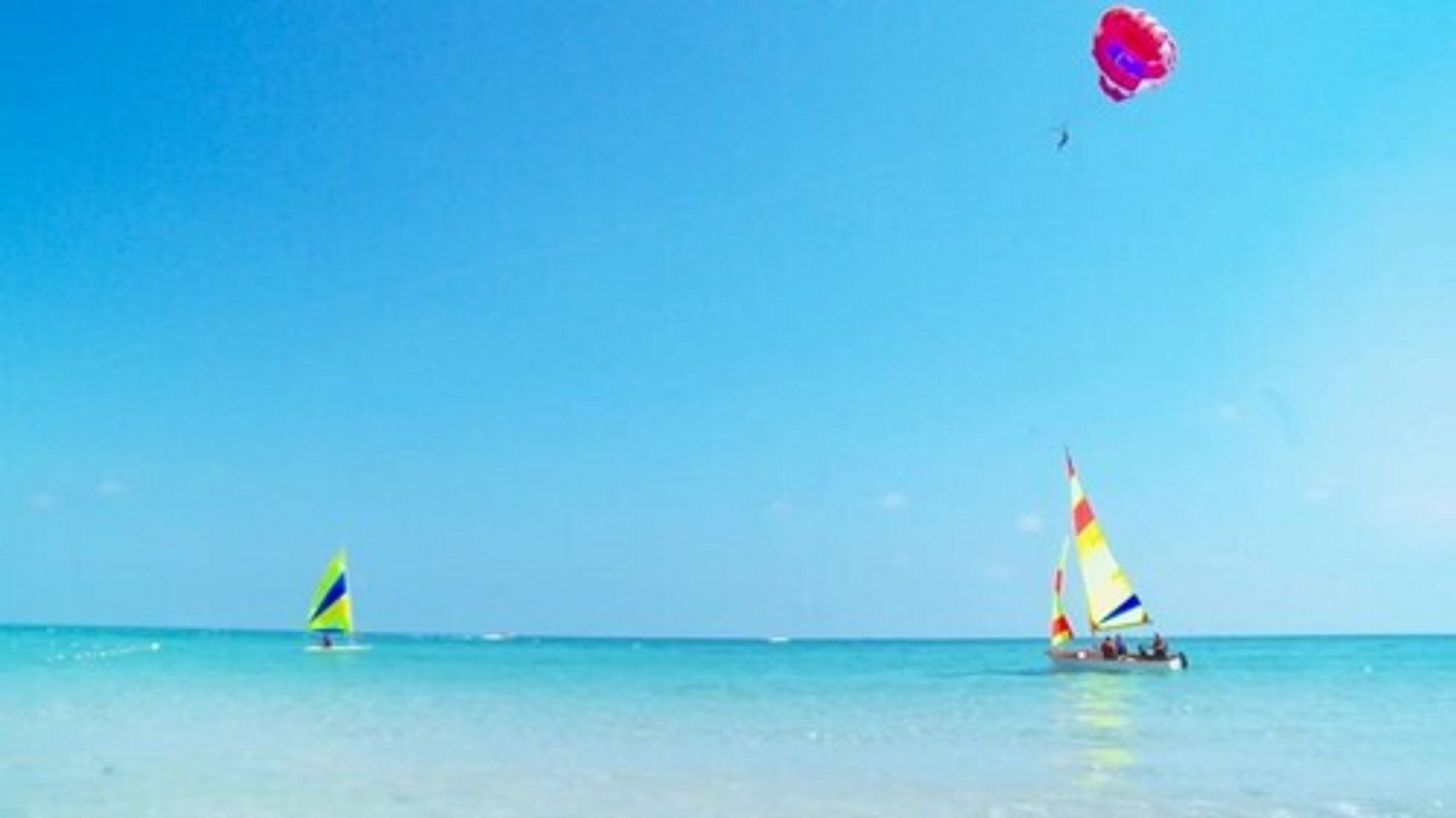 A beach with two sailboats and a kite in the sky.