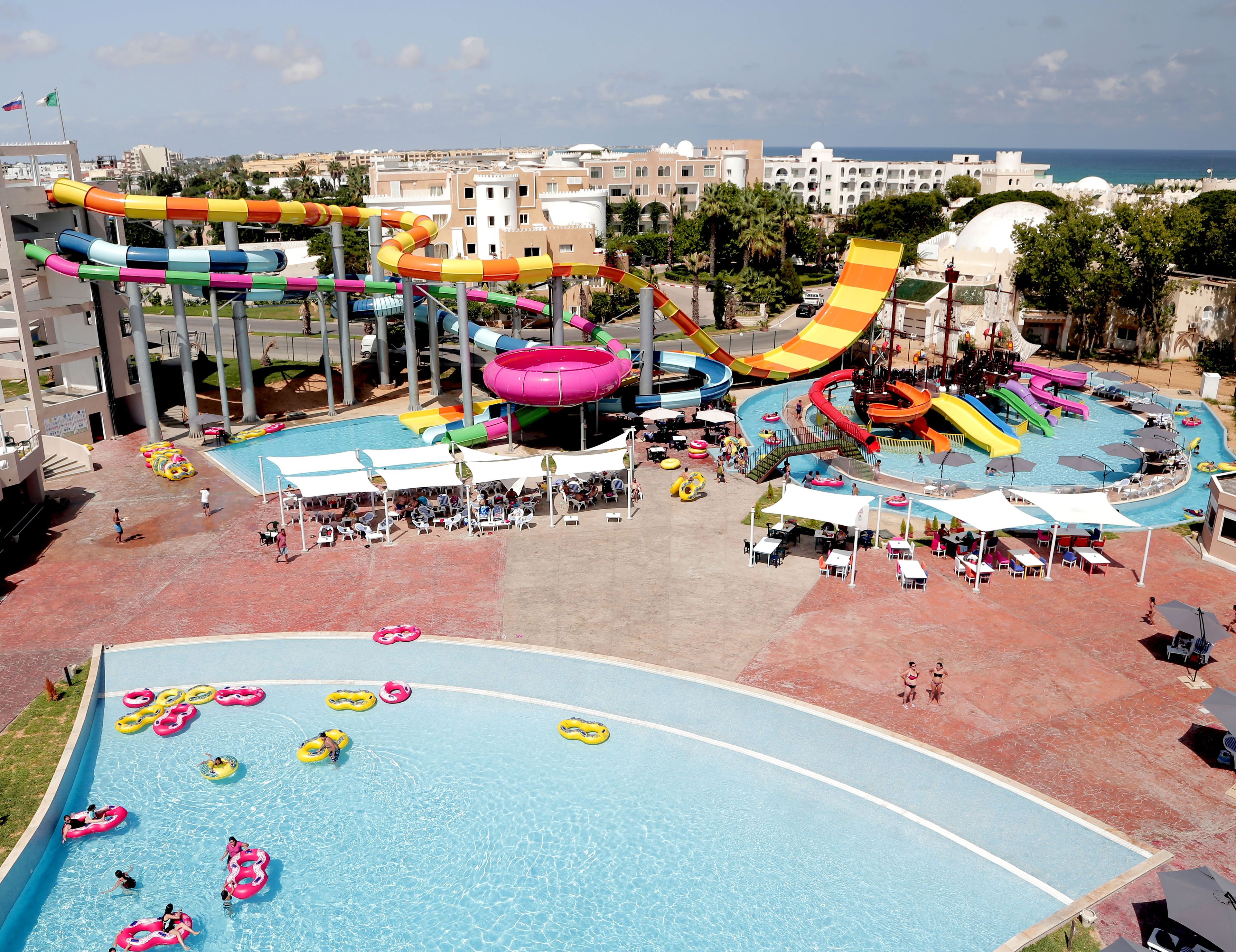 A water park with multiple slides and pools, surrounded by buildings and palm trees.