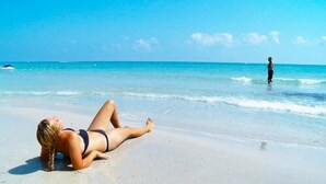 A beach scene with a person lying on the sand and another standing in the water. -  Mahdia beach & aquapark (Mahdia)
