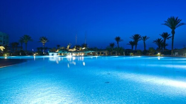 A large, clear swimming pool at night with palm trees and buildings in the background. -  Mahdia beach & aquapark (Mahdia)