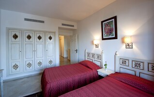 Habitación de hotel con dos camas, un armario blanco, un cuadro en la pared y una mesita de noche con lámpara.