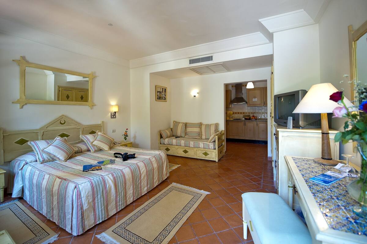 A bedroom with a bed, bedside tables, a sofa, a desk with a lamp, and a mirror.