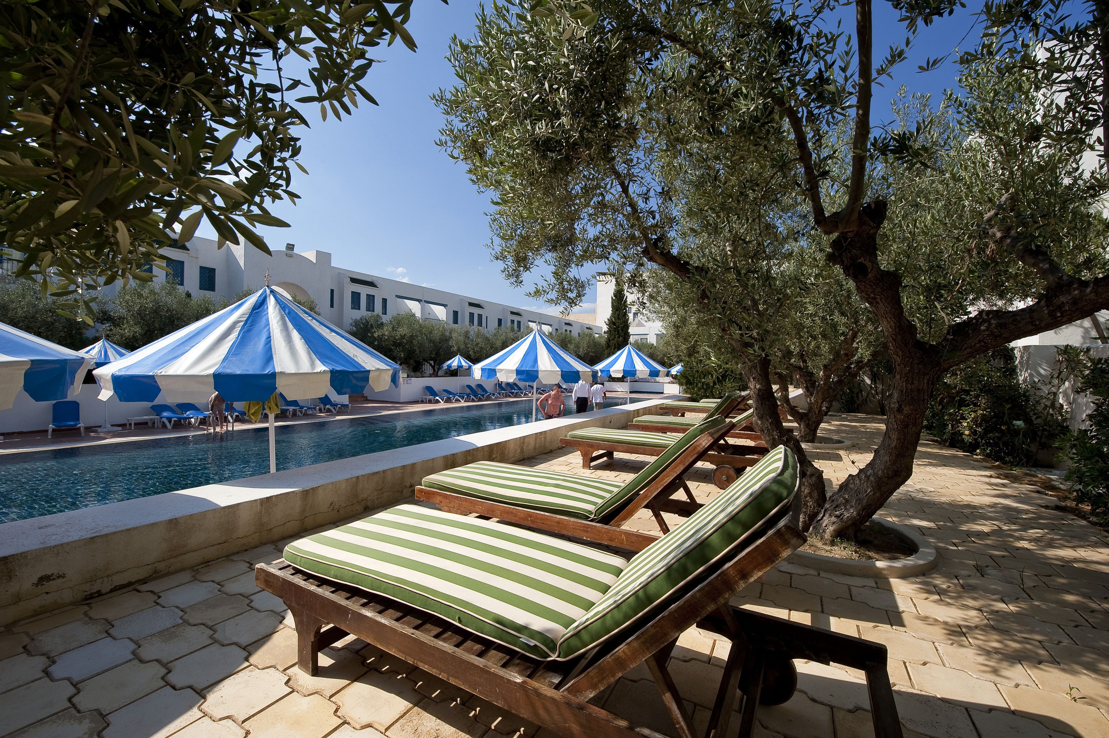 A poolside area with lounge chairs and umbrellas, a swimming pool, and a building in the background.