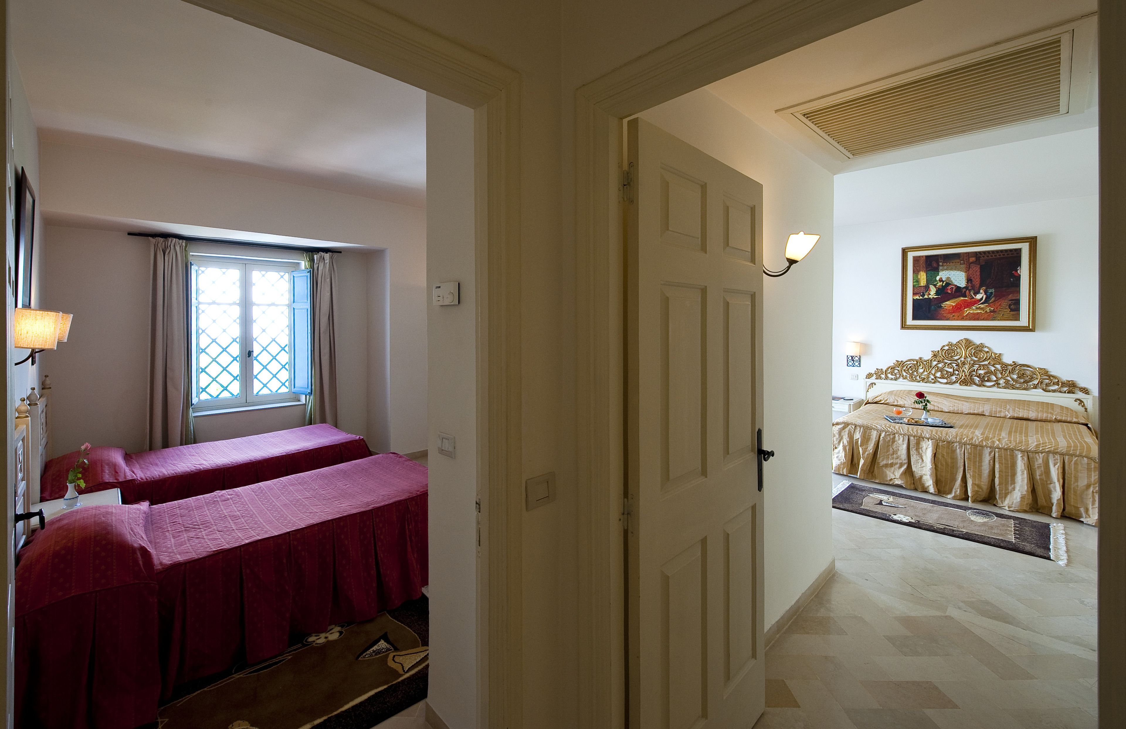 A hotel room with two beds, a window with curtains, a painting on the wall, and a wooden floor.