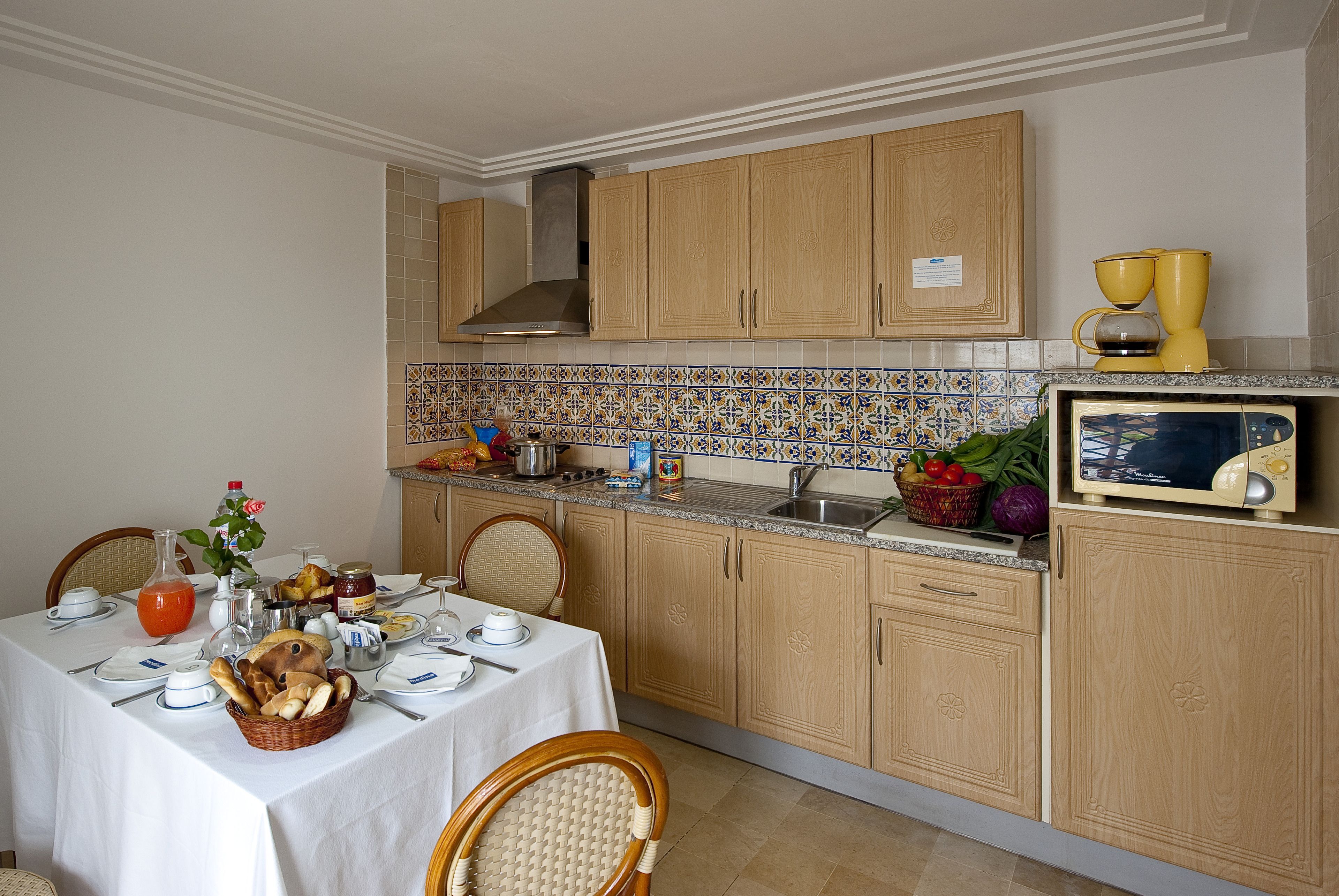A kitchen with wooden cabinets, a tiled backsplash, and a dining table set for a meal.