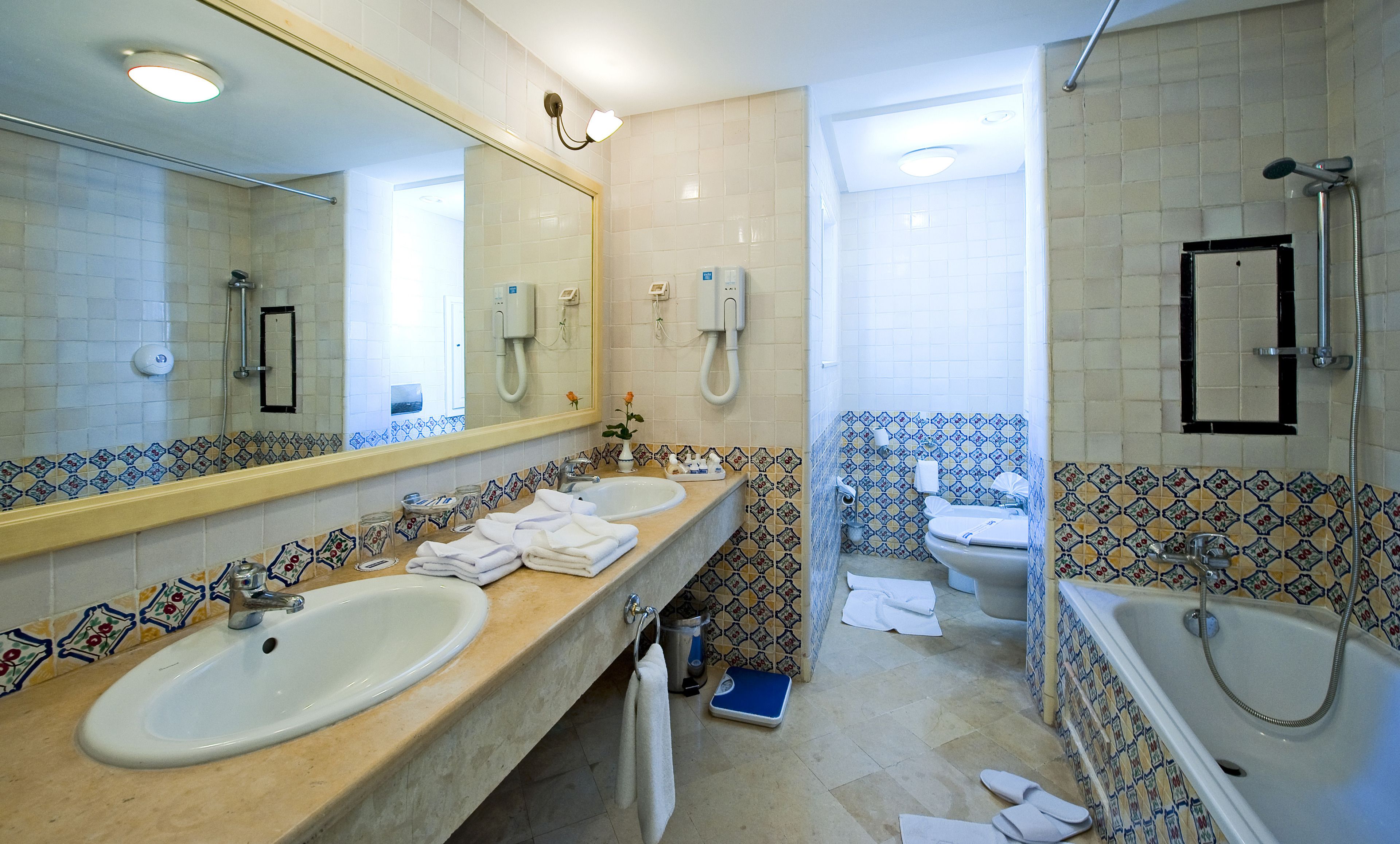 Une salle de bain avec un grand miroir, deux lavabos, une baignoire et des toilettes.