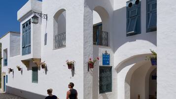 A white building with arched doorways and windows, a cobblestone street, and hanging flower baskets.