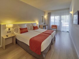Habitación de hotel con dos camas, un escritorio, una silla y un ventanal con cortinas.