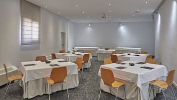 A conference room with multiple tables and chairs, carpeted floor, and ceiling lights.