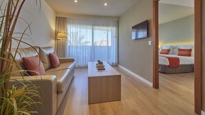A modern hotel room with a sofa, a coffee table, a TV, and a bed with red pillows. - BQ Augusta Hotel (Palma de Mallorca)