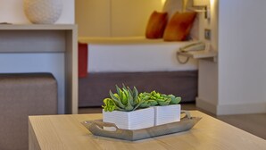 A modern living room with a wooden table, a white planter with succulents, a sofa with orange cushions, and a wall-mounted lamp. - BQ Augusta Hotel (Palma de Mallorca)