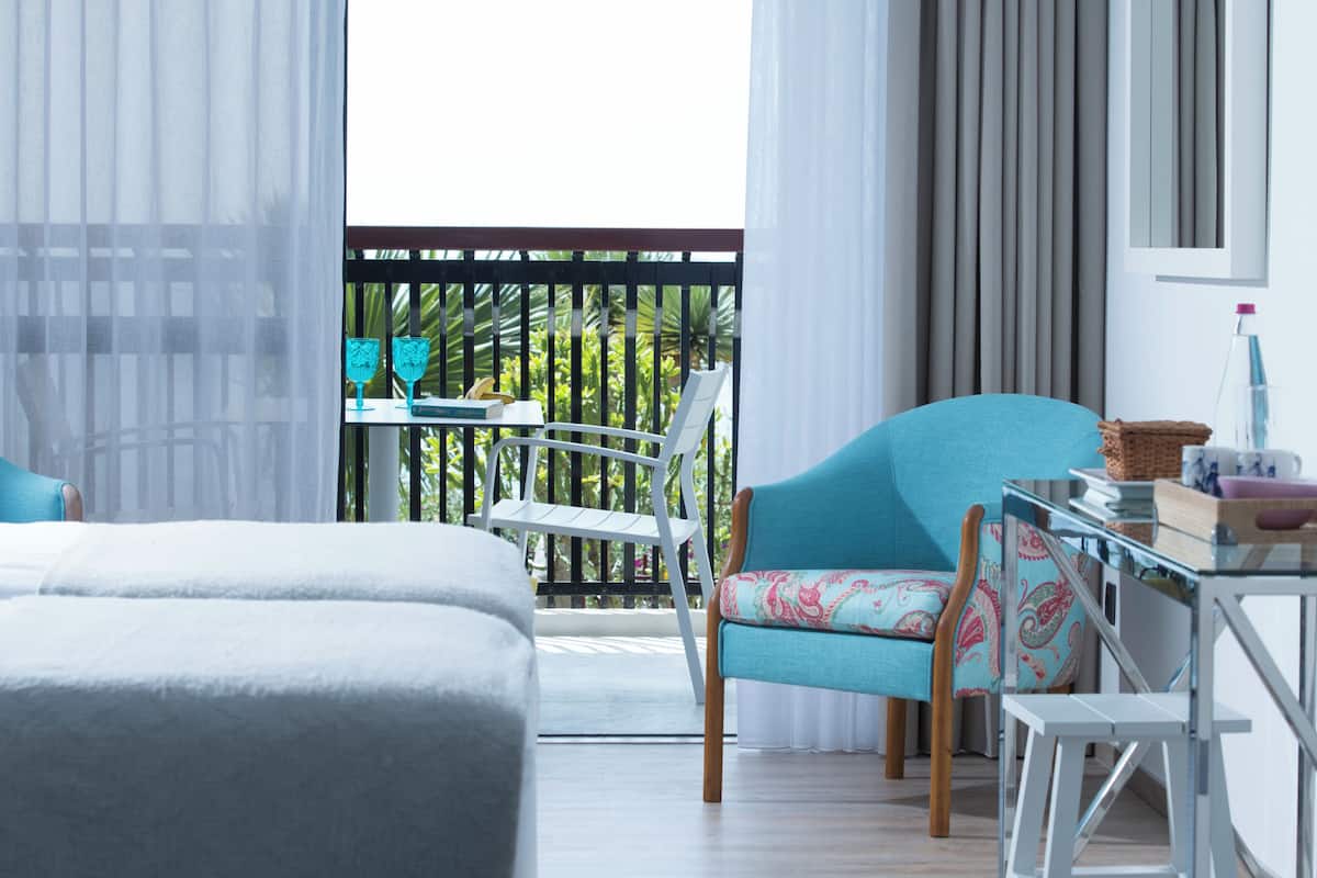Habitación de hotel con balcón, cama, silla, mesa y ventana con cortinas.
